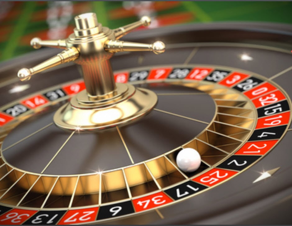 A close-up view of a roulette wheel in a casino. The image shows the golden spindle and ball-track of the wheel, with the numbered pockets visible around the edge. The pockets are alternating red and black, with the numbers clearly visible. A small white ball is seen resting in one of the pockets. The image captures the glossy, reflective surface of the wheel, emphasizing the luxurious and high-stakes nature of the game.